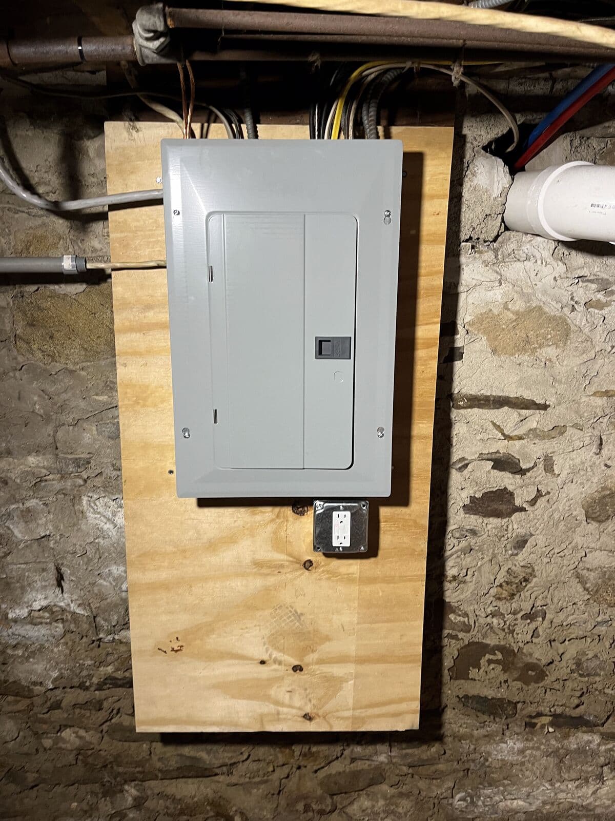 New breaker panel mounted on plywood in a stone basement